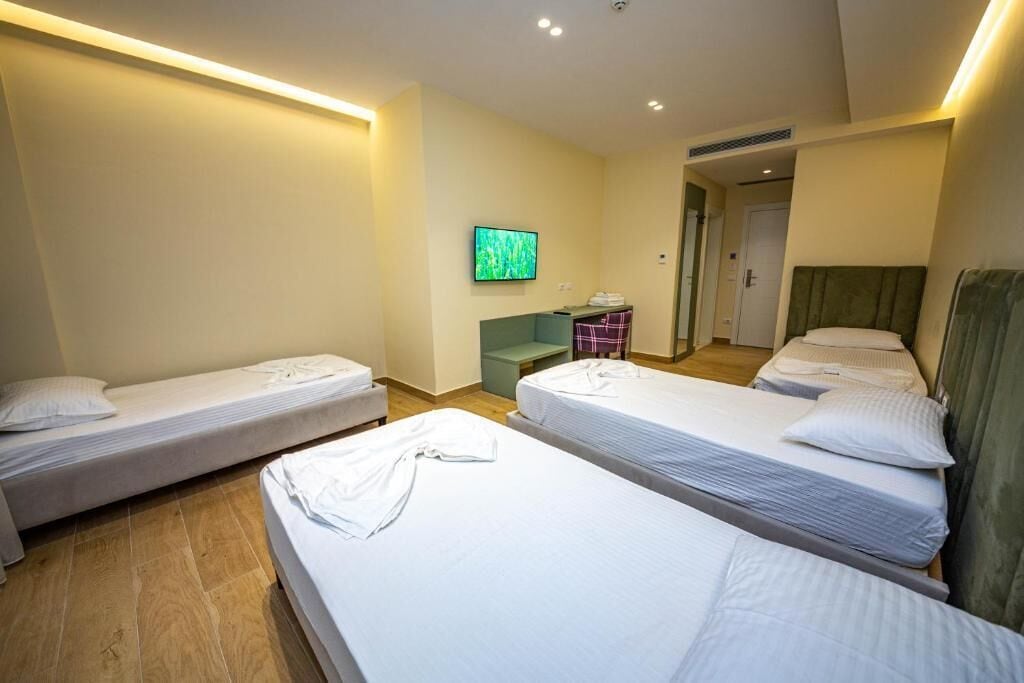 Habitación de hotel con tres camas individuales, un escritorio pequeño, televisión y una puerta que da a otra habitación.
