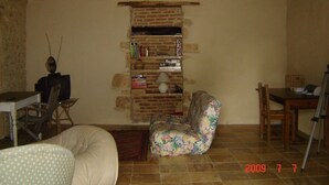 A rustic room with a brick fireplace, a floral armchair, a wooden table, and a television. - 2 Beautiful country houses fully restored - stunning view                 (Dordogne)