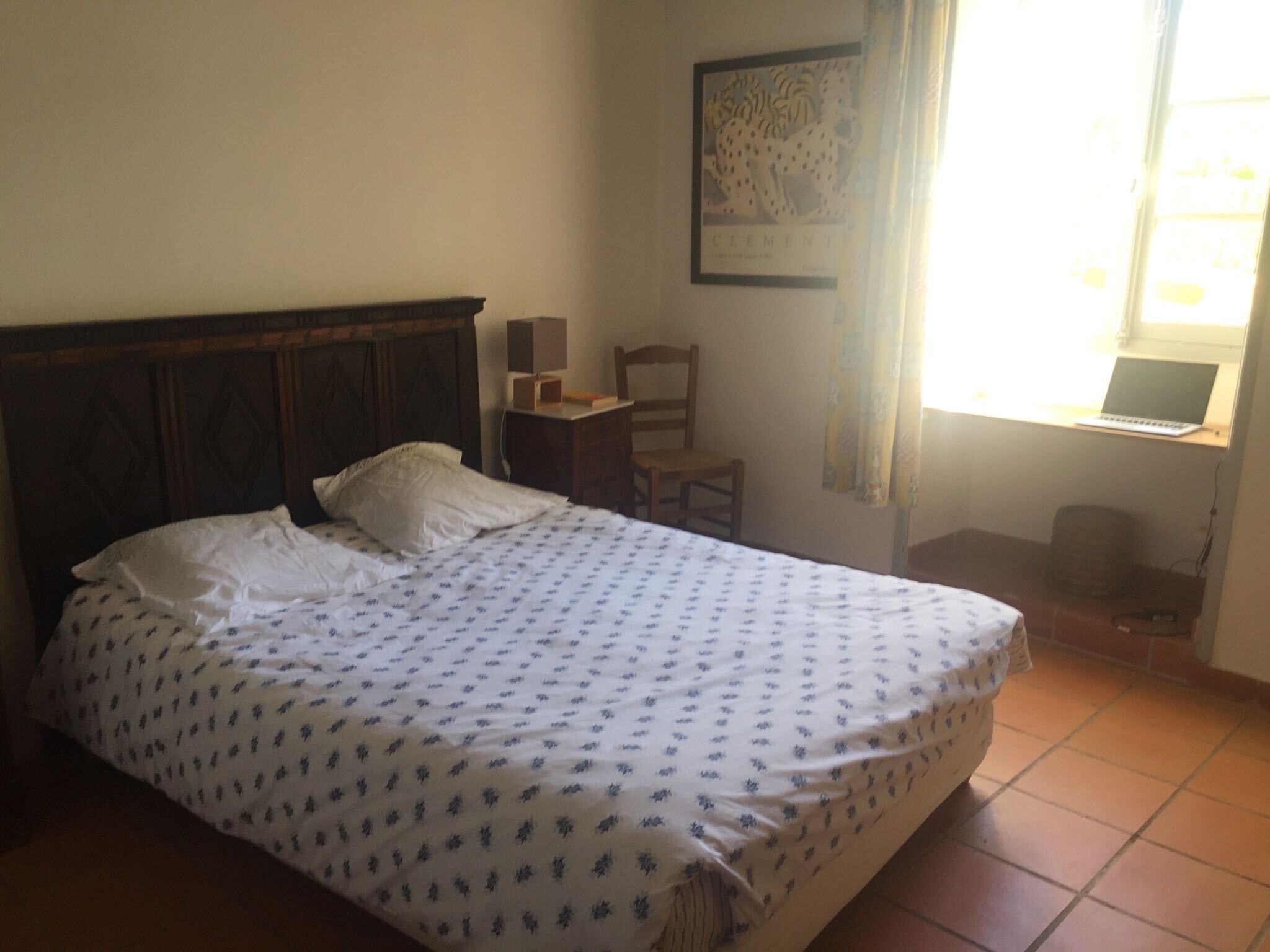 Une chambre à coucher avec un lit, une chaise, un bureau, un ordinateur portable et un tableau encadré au mur.