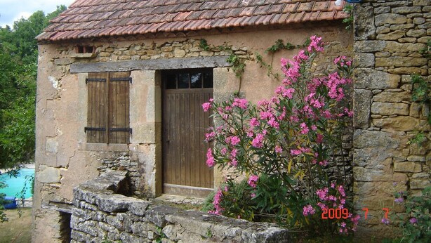 A rustic stone building with a tiled roof, a wooden door, and pink flowering plants in front. - 2 Beautiful country houses fully restored - stunning view                 (Dordogne)