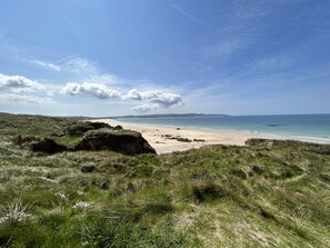 Et kystlandskab med græsarealer, der fører ned til en sandstrand og havet.