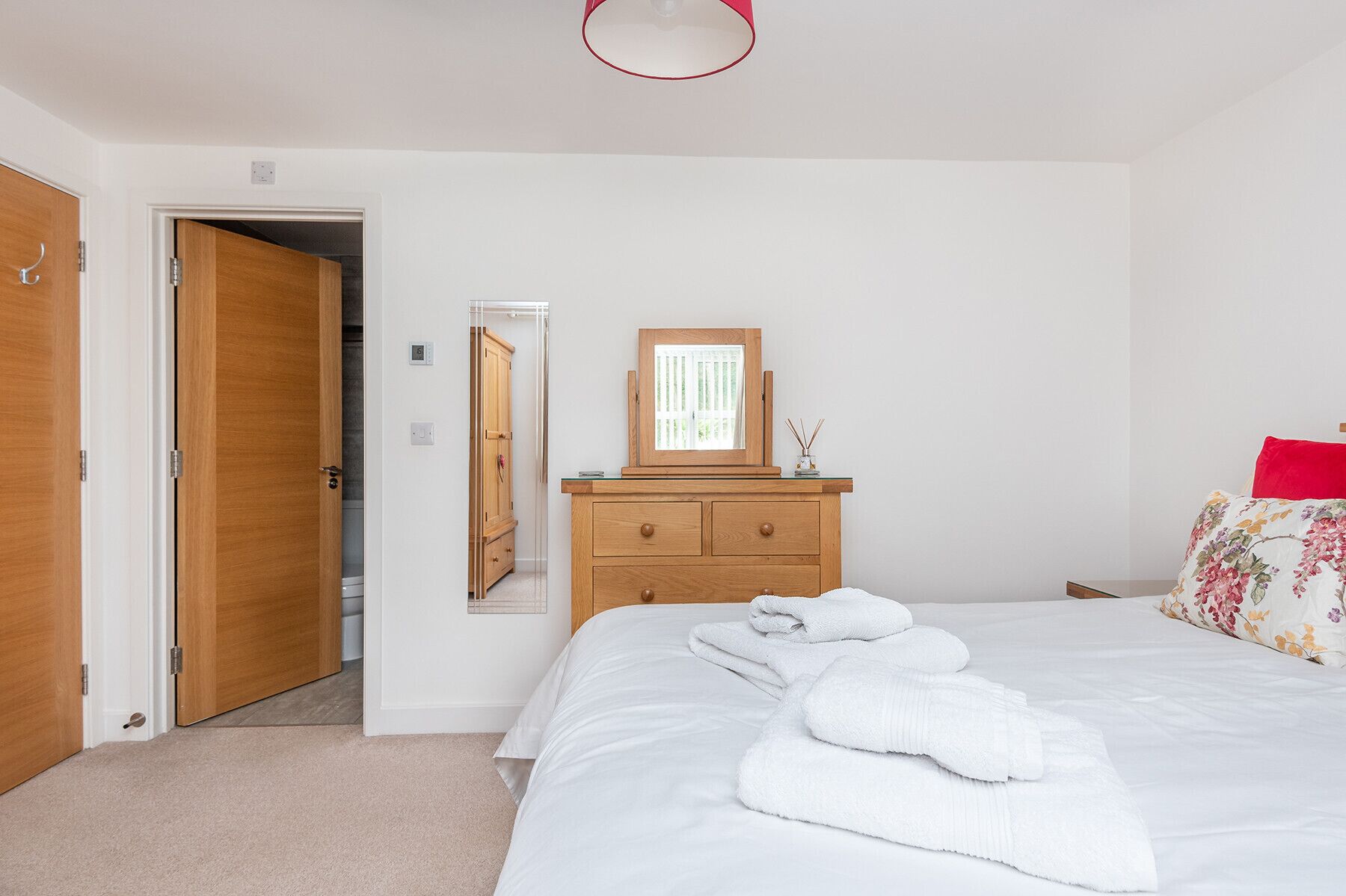 Ein Schlafzimmer mit einem Bett, einer Holzkommode, einem Spiegel und einer Tür zu einem Badezimmer.