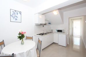 A compact kitchen with white cabinetry, a microwave, and a gas stove. There is a dining table with chairs and a vase of flowers.