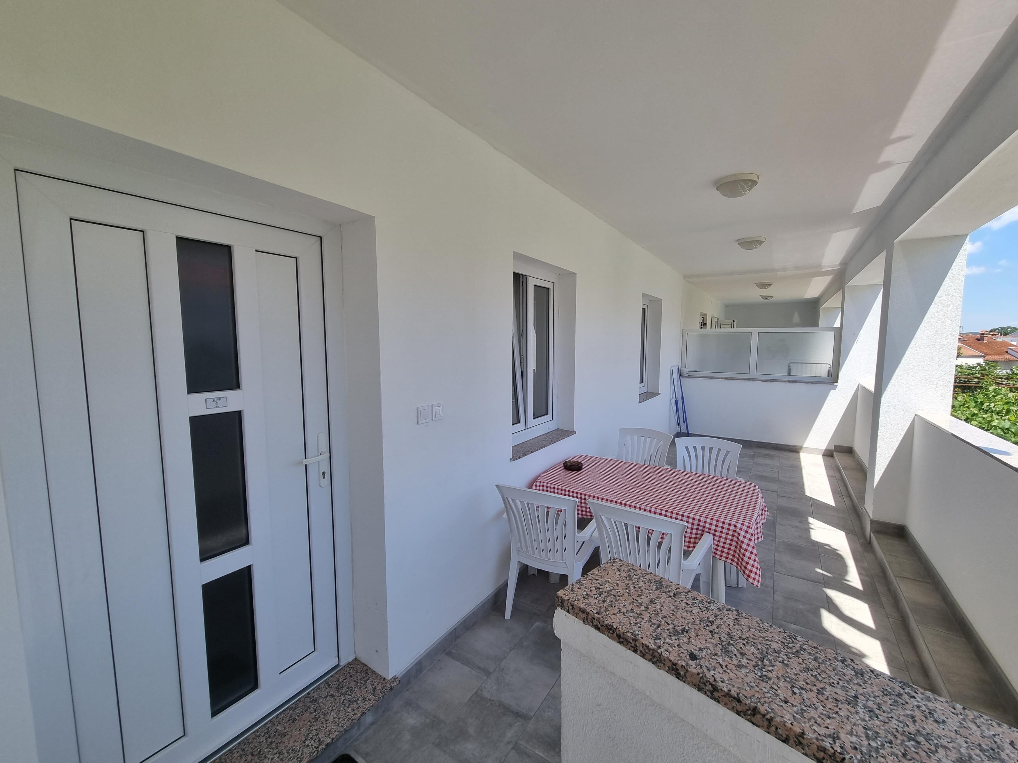A balcony with a table and chairs, a door, and a kitchen area in the background.