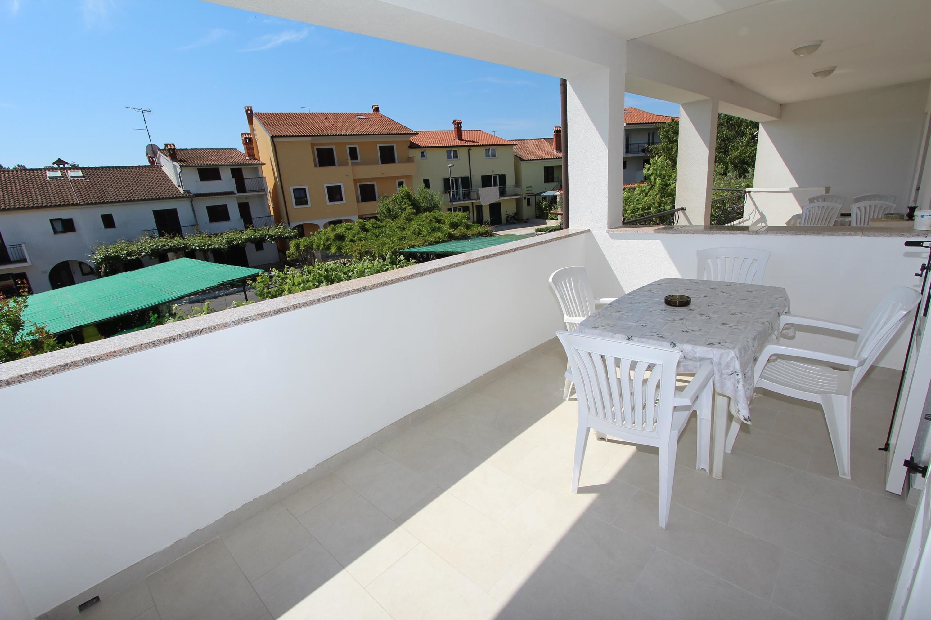 Un balcon avec une table et des chaises, donnant sur un quartier résidentiel avec des immeubles et de la verdure.