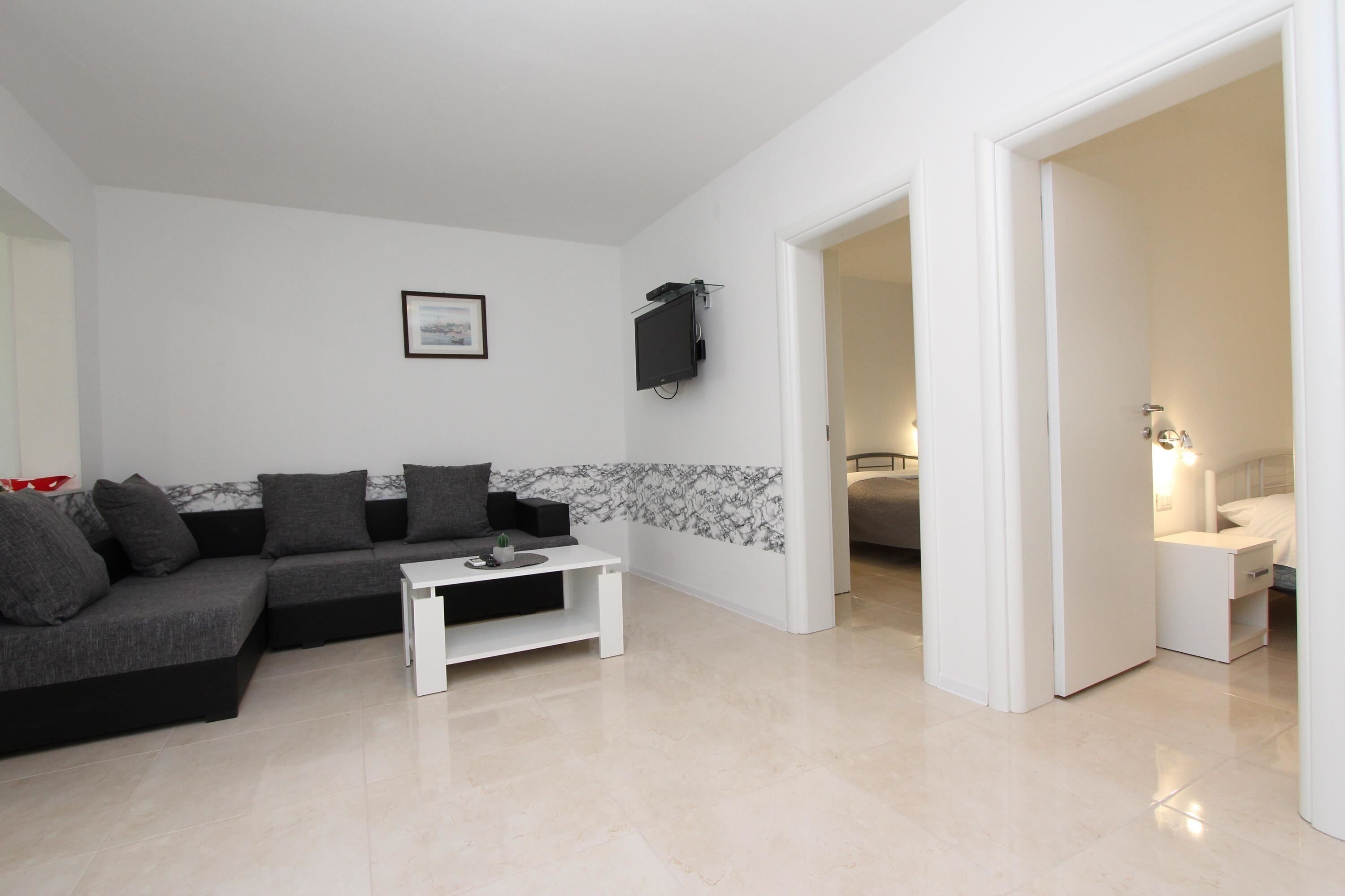 Una sala de estar moderna con un sofá seccional, una mesa de centro blanca y un televisor de pantalla plana montado en la pared.