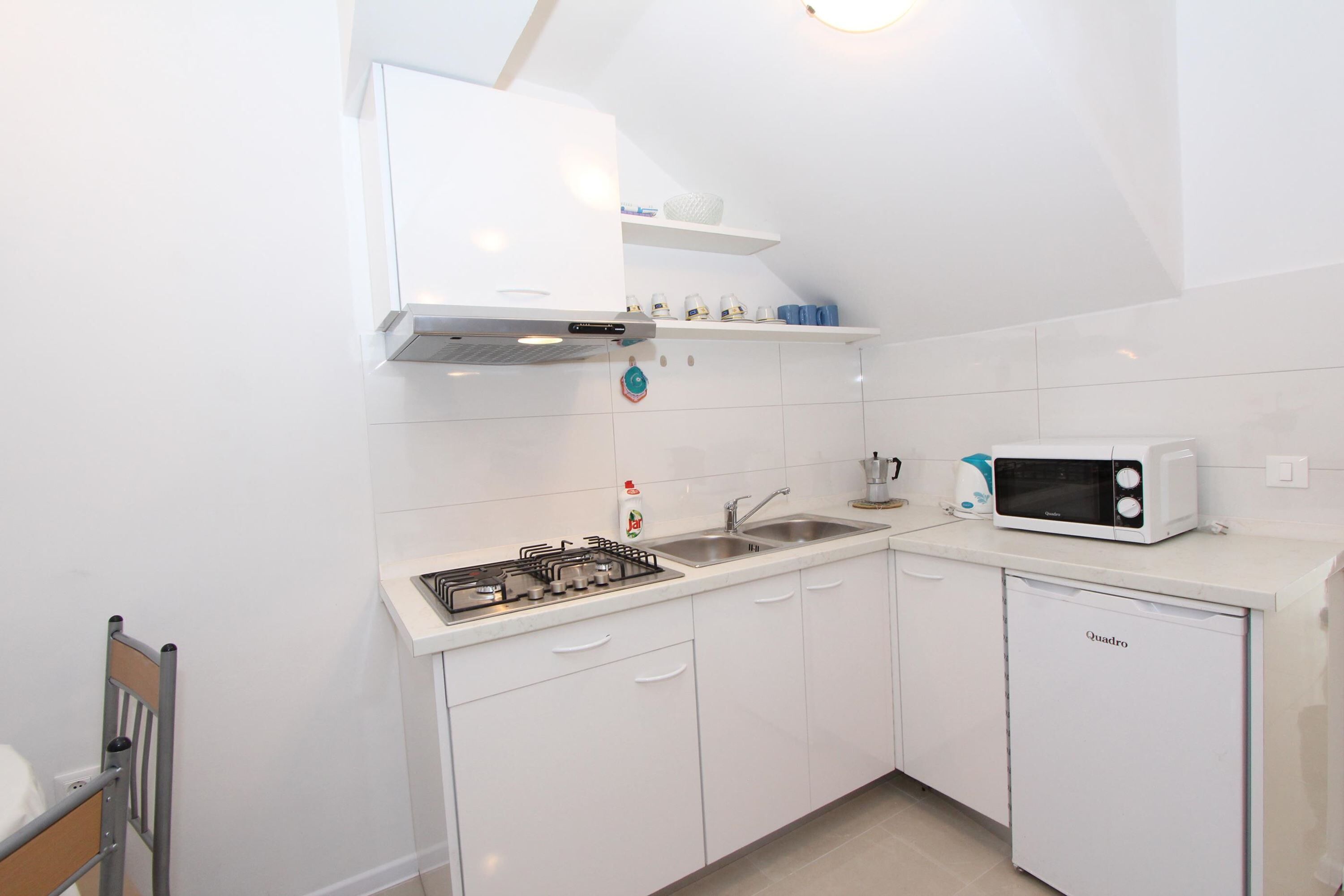 A compact kitchen with white cabinets, a gas stove, a microwave, and a sink.