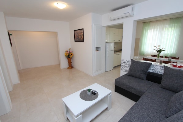A modern living room with a grey sofa, a white coffee table, and a kitchen area visible through an open door.