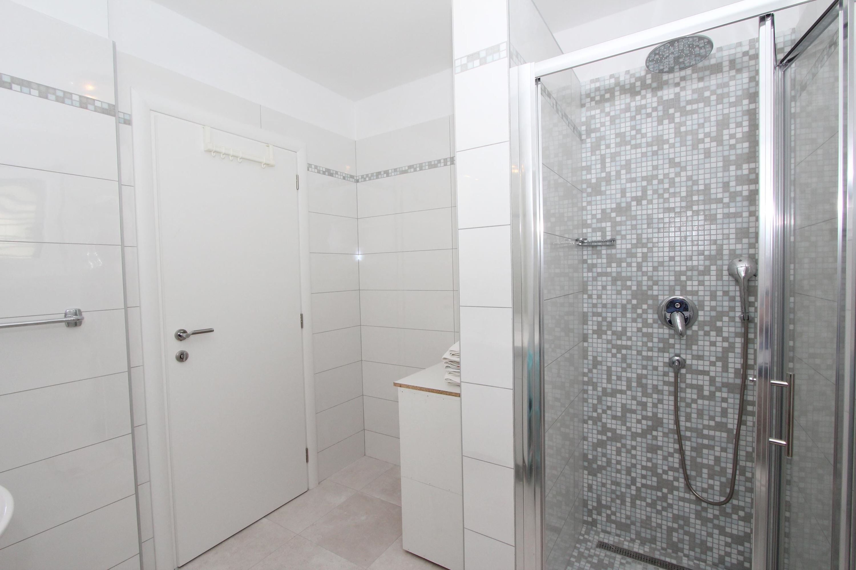 Um banheiro moderno com chuveiro em box de vidro, paredes com azulejos brancos e vaso sanitário visível.
