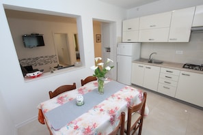 A dining area with a table set for two, a vase with flowers, and a kitchen with white cabinets and a sink.