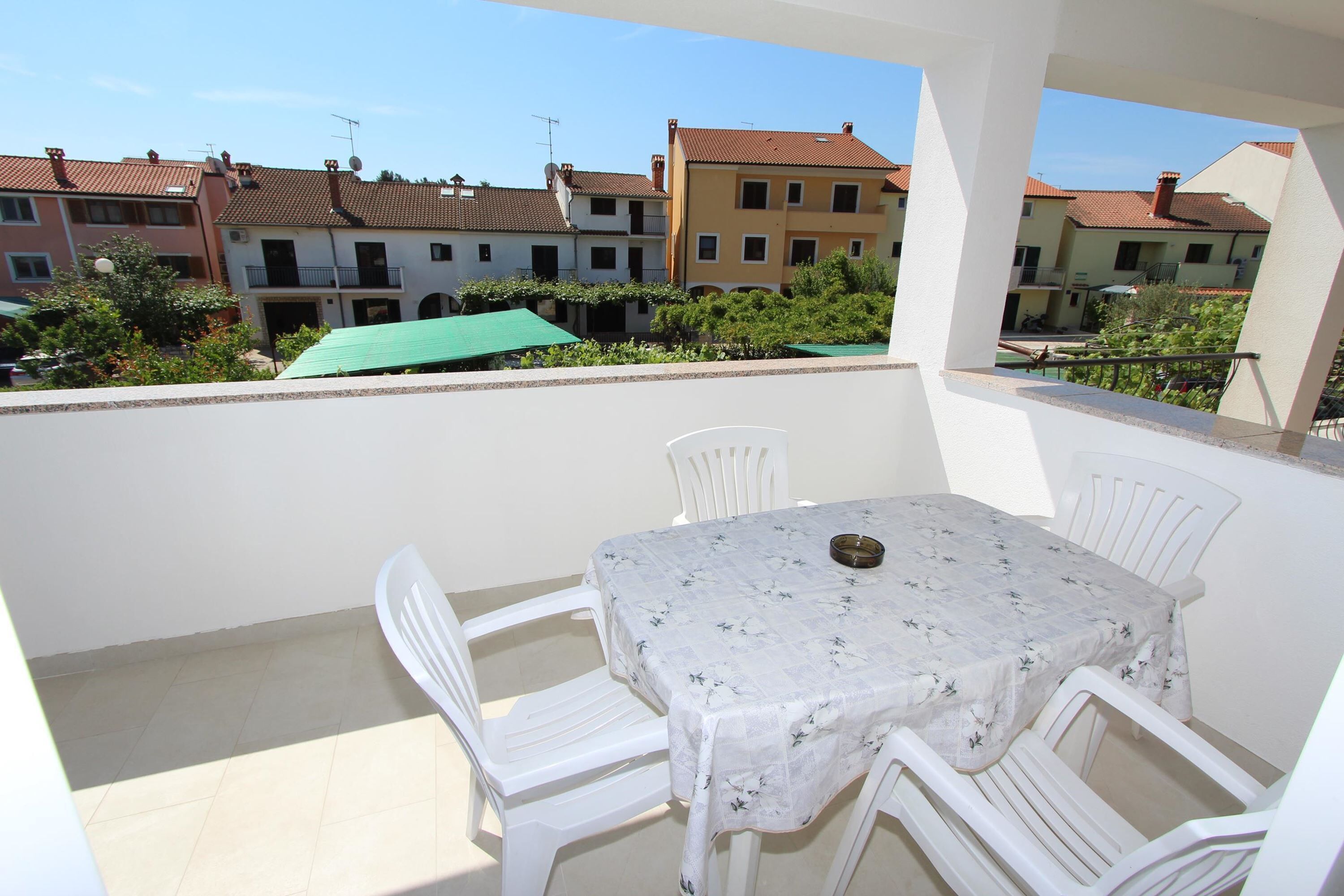 A balcony with a table and chairs, overlooking a row of buildings with red-tiled roofs.