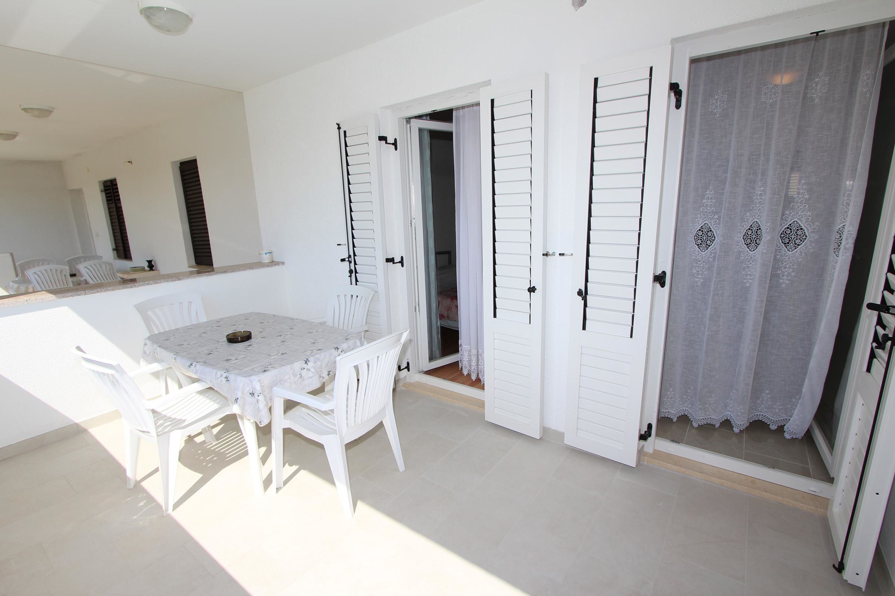 Una habitación con una mesa y sillas blancas, un espejo y una puerta con cortina blanca.