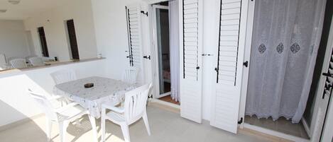Una habitación con una mesa y sillas blancas, un espejo y una puerta con cortina blanca.