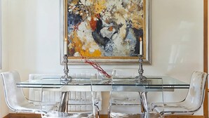 A dining area with a glass table and chrome chairs, a large abstract painting on the wall, and a vase with dried flowers on the table. - Exquisite designer 3BR Pg Gràcia apt - LaMimosa (Barcelona)