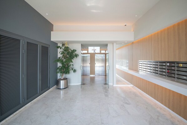 A modern hallway with a potted plant, a reception desk, and a row of lockers. - Sea View three bedroom apartment in Garcia Faria - You Stylish (Barcelona)