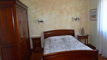 A bedroom with a wooden bed, two bedside tables, a nightstand, a wardrobe, and wall-mounted lamps.