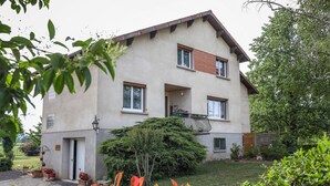 Ein zweigeschossiges Gebäude mit Balkon, einer Tür und einem kleinen Gartenbereich mit Blumentöpfen.