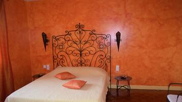 A bedroom with an orange wall, a decorative metal headboard, two pillows, a small round table, and a chair.