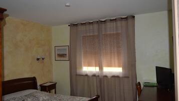 Un dormitorio con cama, escritorio y ventana con cortinas.