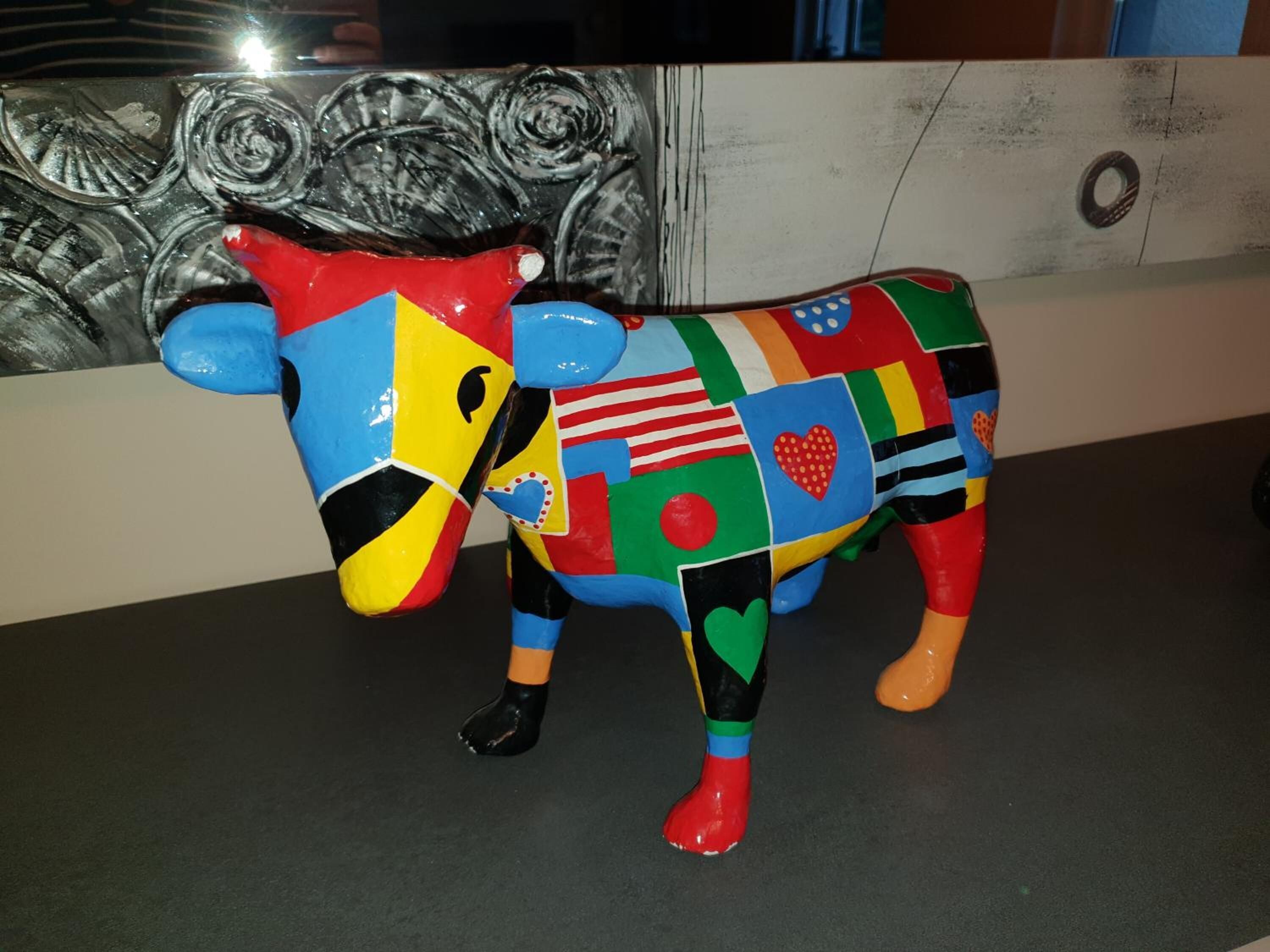 A colorful, abstract sculpture of a cow on a dark floor.