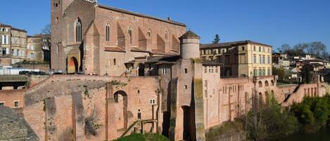 Un edificio histórico con una torre destacada, ventanas de arco y una muralla fortificada que da vista a un río.