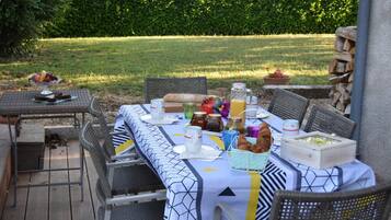 An outdoor dining area with a table set for a meal, surrounded by wicker chairs, and a view of a well-maintained lawn and hedge in the background.