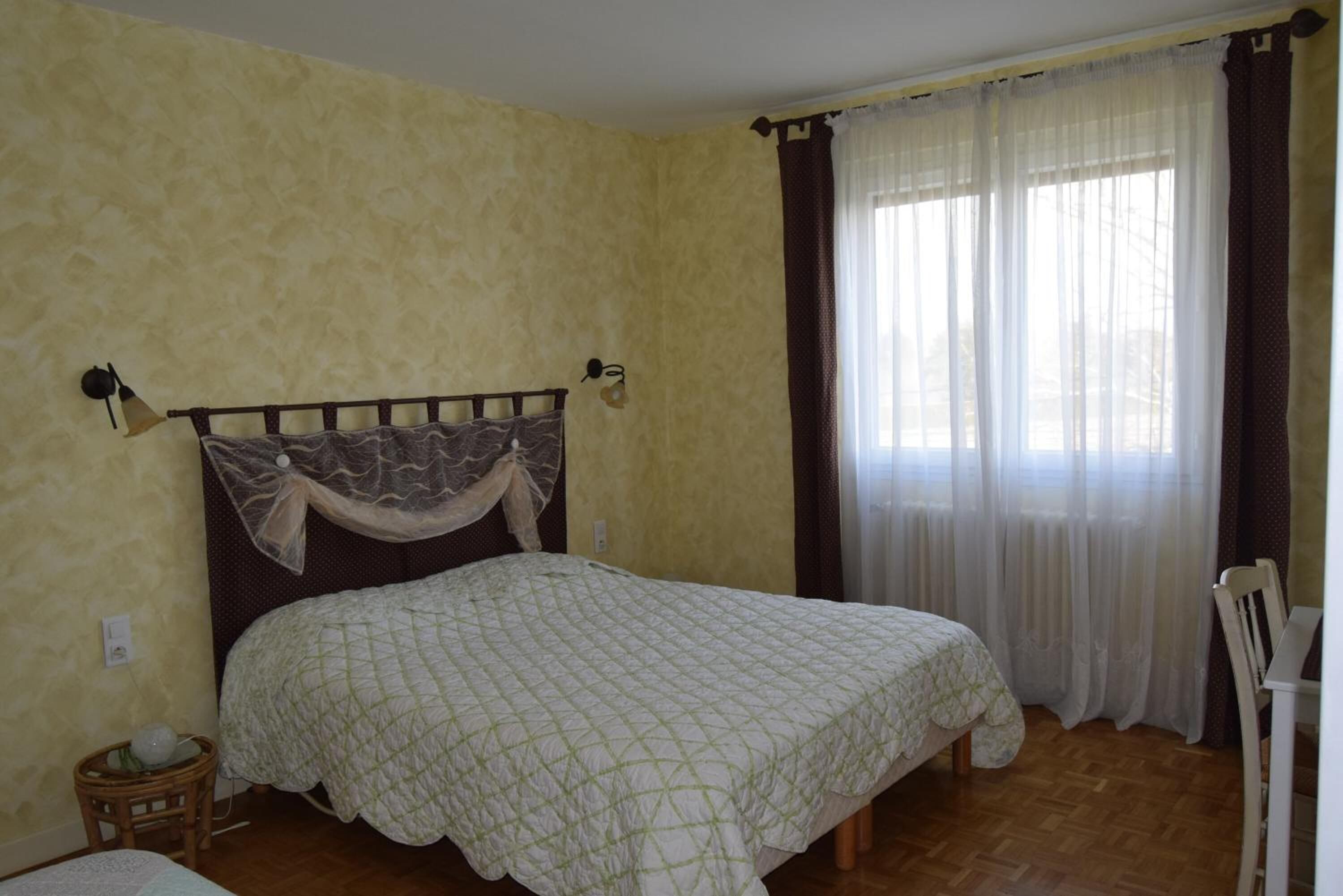 Un dormitorio con cama, mesita de noche, lámpara y ventana con cortinas.