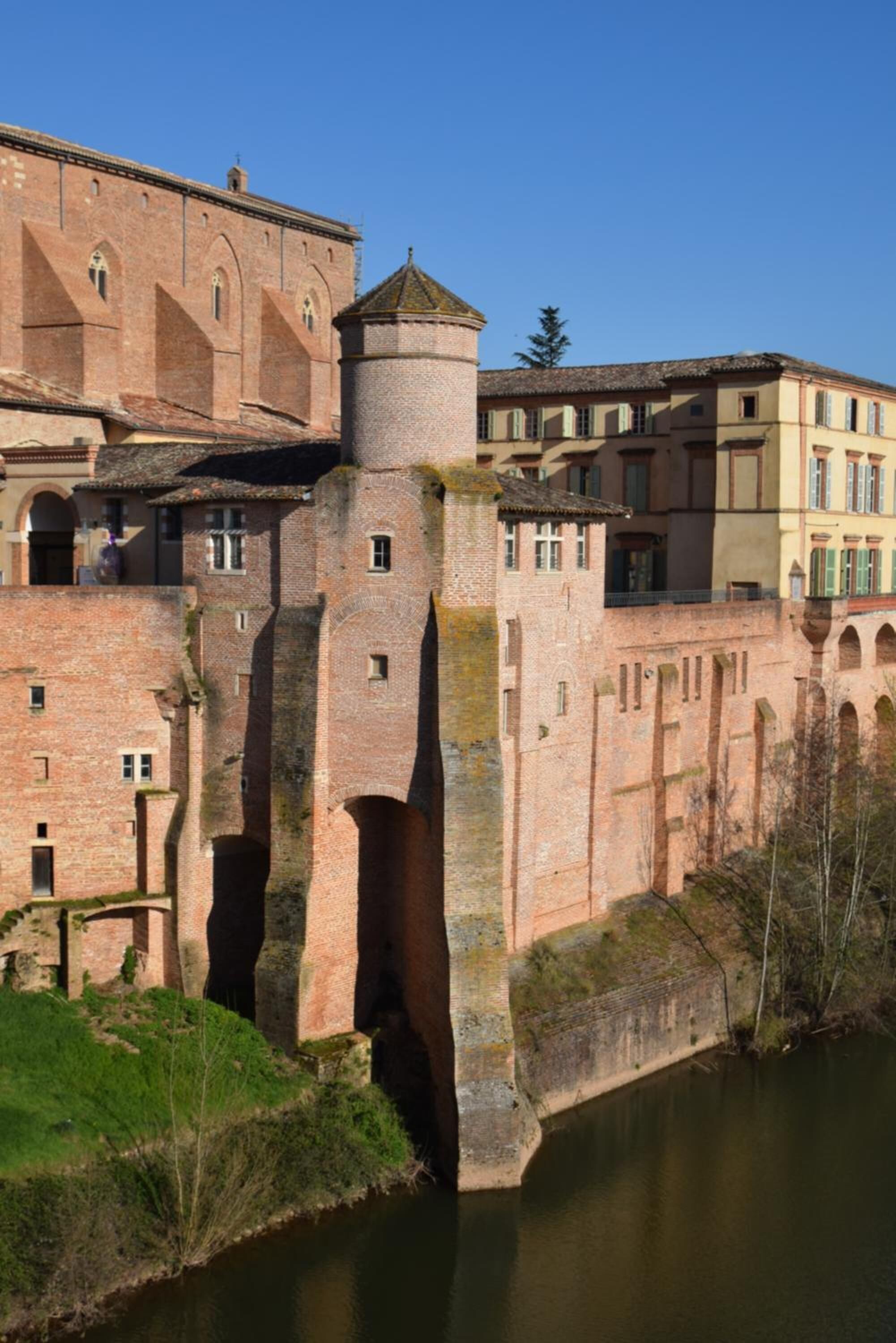 A historic building with a prominent tower and a fortified wall by a river.