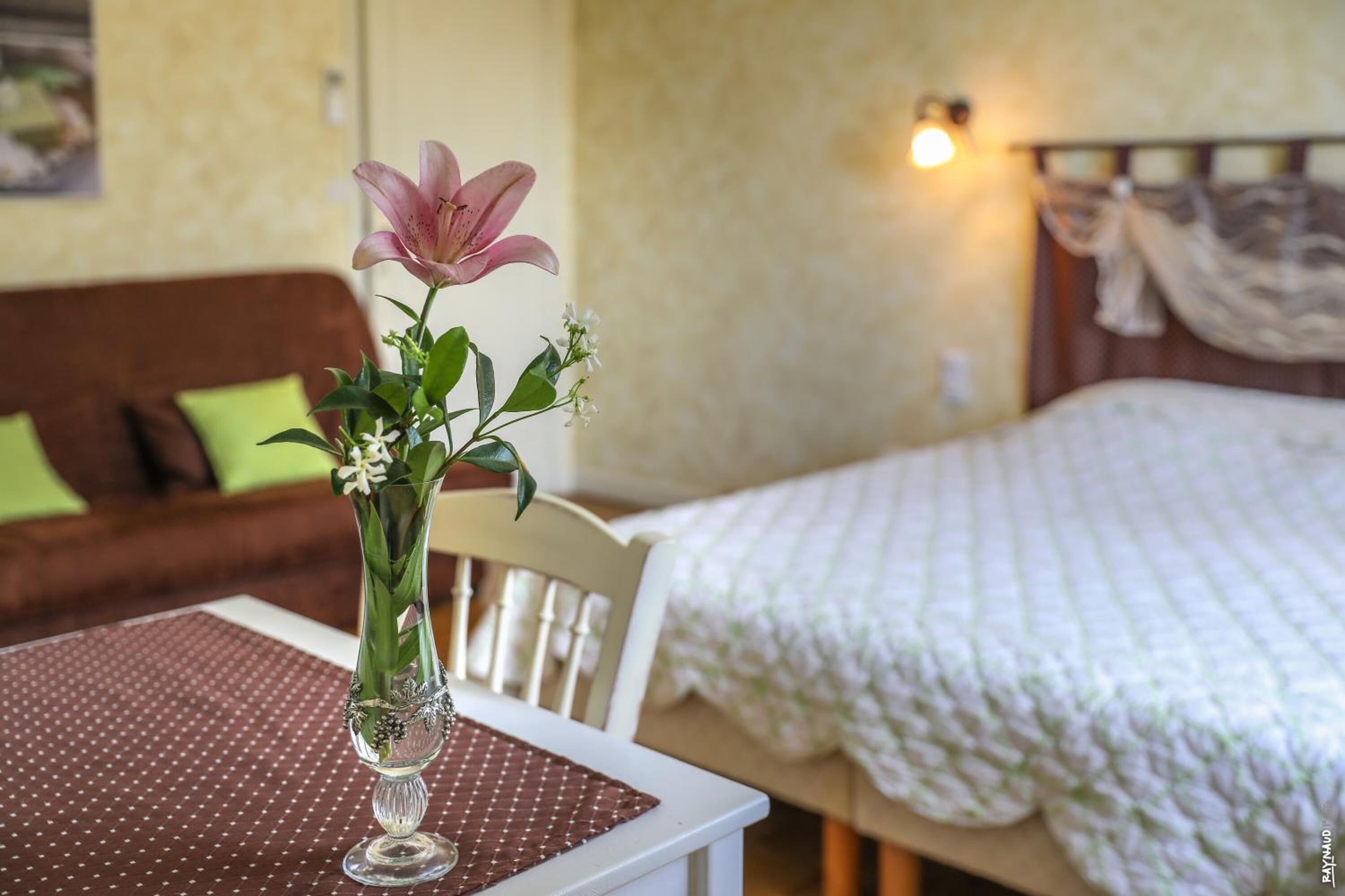 Una habitación con una cama, una silla y una mesa con un jarrón de flores.