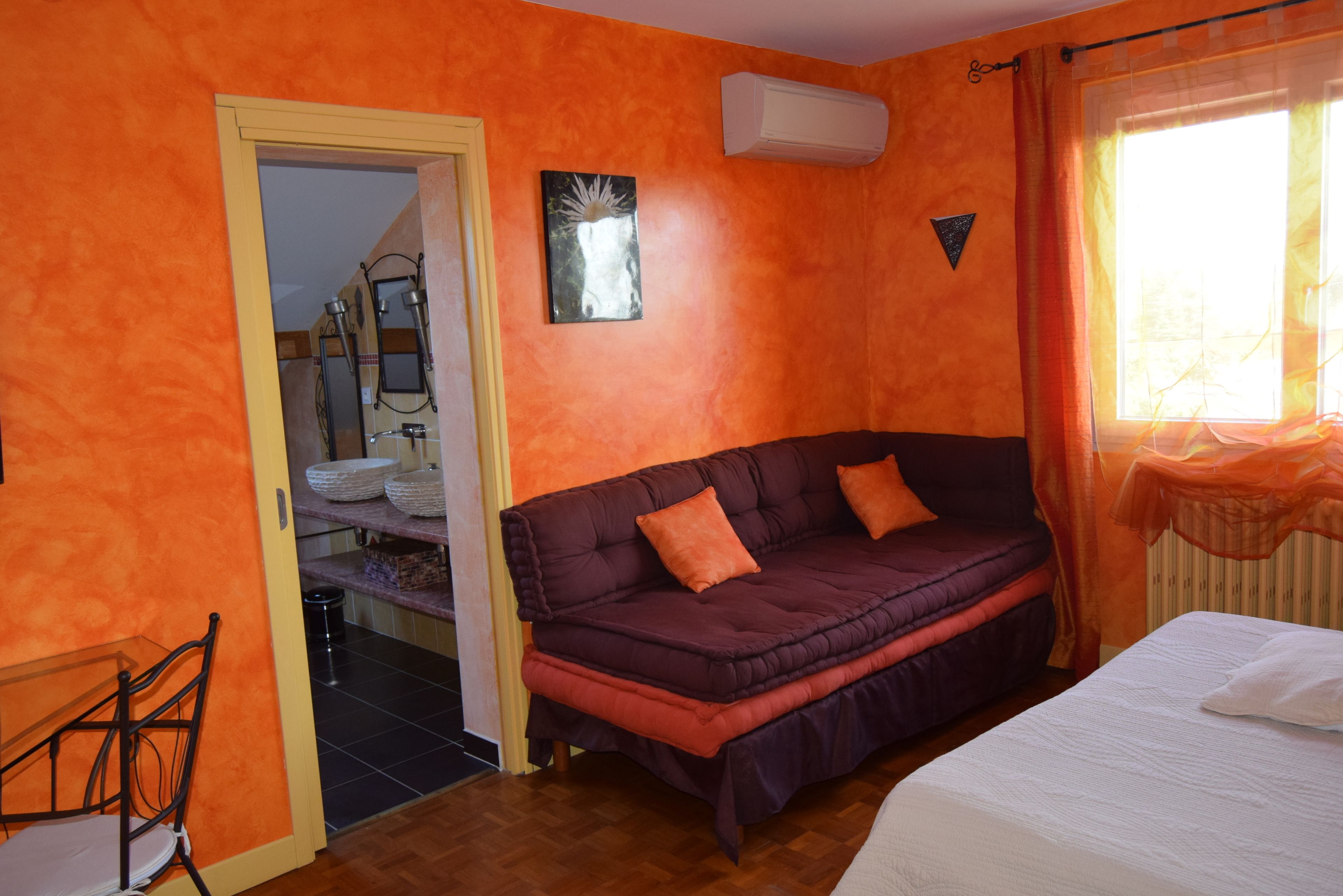 A room with a bed, a sofa, a chair, an air conditioning unit, and a window with curtains.