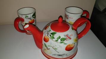 A white teapot with red handles and a matching cup set with apple designs.