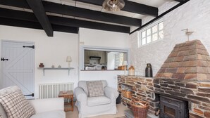 Un accogliente soggiorno con camino, divani bianchi, un tavolino in legno e vista sulla cucina attraverso una finestra.