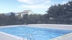 Une piscine rectangulaire dont le bord est recouvert de carreaux, entourée d’une zone pavée et d’une clôture.