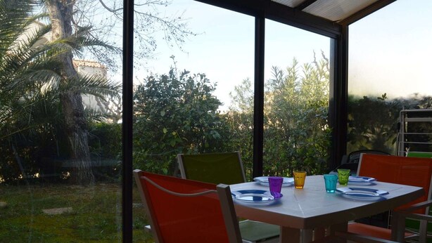 Un espace repas comprenant une table et des chaises, de grandes fenêtres et une vue sur la verdure.