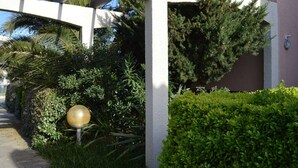 Une allée couverte, surmontée d’un luminaire sphérique, entourée d’une végétation luxuriante et bordée par la façade d’un bâtiment.
