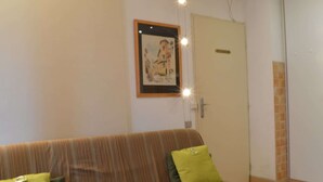 Un salon avec un canapé à rayures, deux coussins verts, un tableau encadré au mur et une porte fermée.