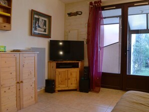Ein Zimmer mit einem Holzschrank, einem Fernseher auf einem Holzbodenständchen, einer Box und einem Fenster mit Vorhang.