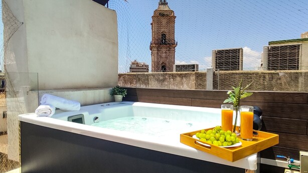 Un jacuzzi en la azotea con una bandeja de uvas y jugo de naranja, una toalla y una planta en maceta.
