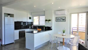 A modern kitchen with white cabinets, a black countertop, and a dining area with a white table and clear chairs. - Playa d'Aro,2 bedrooms, 2 bathrooms, sea view, air conditioning, large terrace, free wifi, private parking (Platja d'Aro)