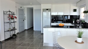 A modern kitchen with white cabinets, a black countertop, and a dining area with a round table. - Playa d'Aro,2 bedrooms, 2 bathrooms, sea view, air conditioning, large terrace, free wifi, private parking (Platja d'Aro)