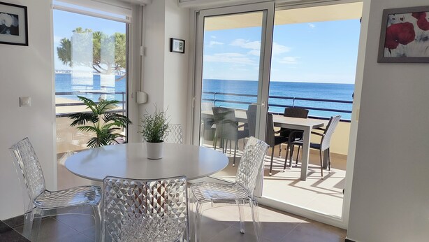 A modern room with a round table and chairs, large windows with a view of the sea, and a balcony with outdoor seating. - Playa d'Aro,2 bedrooms, 2 bathrooms, sea view, air conditioning, large terrace, free wifi, private parking (Platja d'Aro)