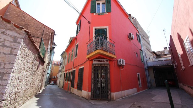 A narrow street with a red building labeled "FRISEUR" and a stone wall on one side. - Studio Pupa (Rovinj)