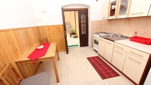 A compact kitchen with wooden cabinetry, a dining table with a red placemat, and a small stool. - Studio Pupa (Rovinj)