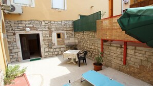 A small outdoor patio with a table and chairs, a potted plant, and a blue lounge chair. - Studio Pupa (Rovinj)