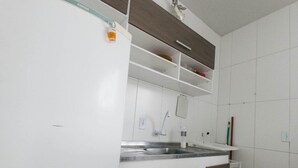 A modern kitchen with white cabinets, a stainless steel sink, and wooden upper cabinets. - Bruno Henning - Apto 6 pessoas (Itapema)