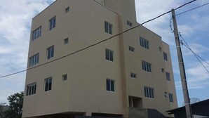 A multi-story building with a flat facade, multiple windows, and a visible utility pole. - Bruno Henning - Apto 6 pessoas (Itapema)