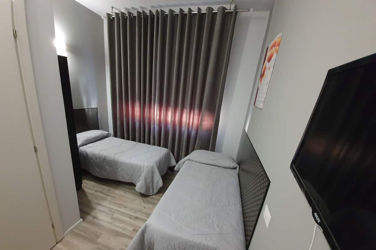 Ett hotellrum med två separata sängar, en tv och en gardin.