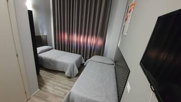 Ett hotellrum med två separata sängar, en tv och en gardin.