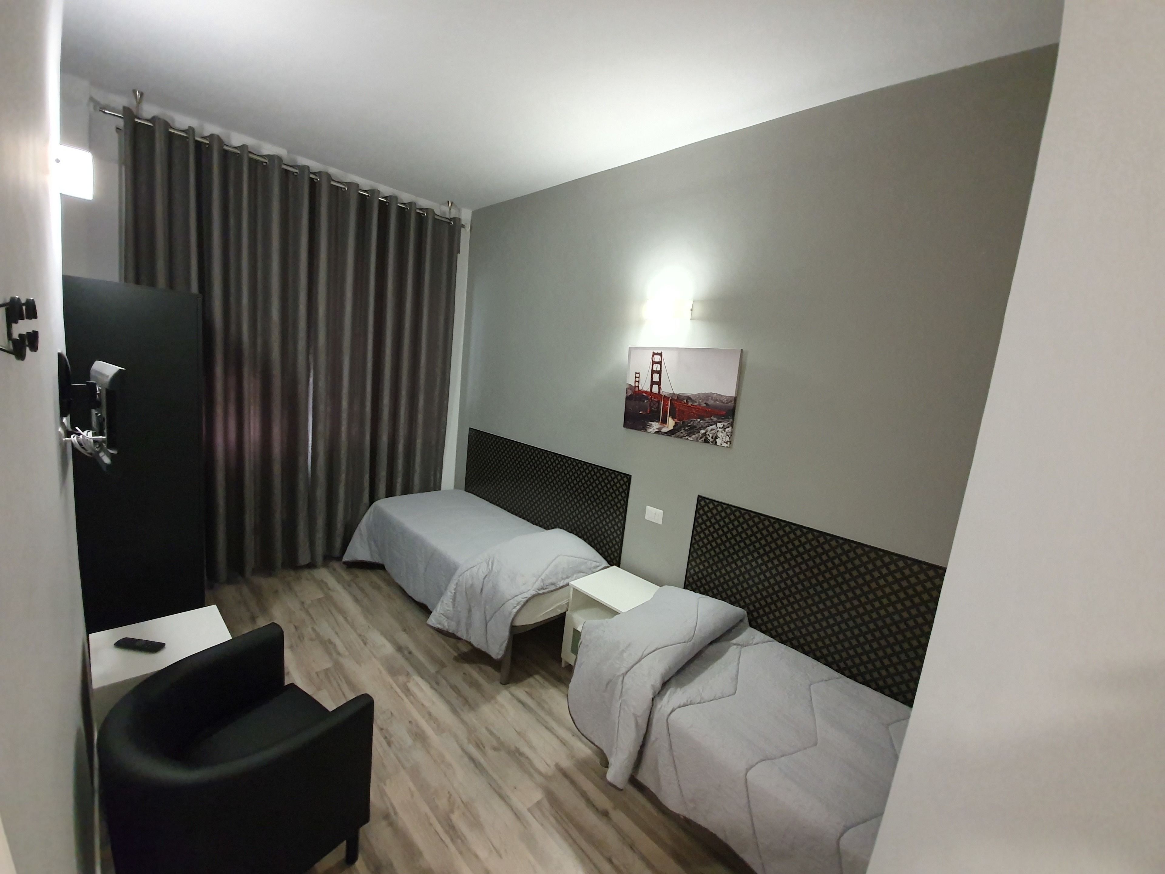 A hotel room with two single beds, a desk, a chair, a curtain, and a wall-mounted picture.