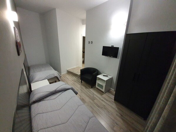 Una habitación compacta con dos camas individuales, un pequeño espacio para sentarse, un televisor montado en la pared y un armario.